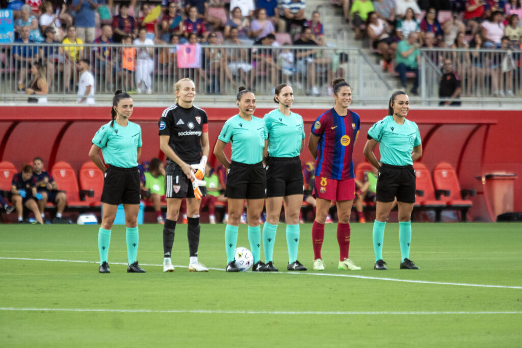 Las capitanas Marta Torrejón y Esther Sullastres, capitanas de Barcelona y Sevilla, y el cuarteto arbitral, en un partido de la Liga 2026-27. Foto: Hugo Mesonero